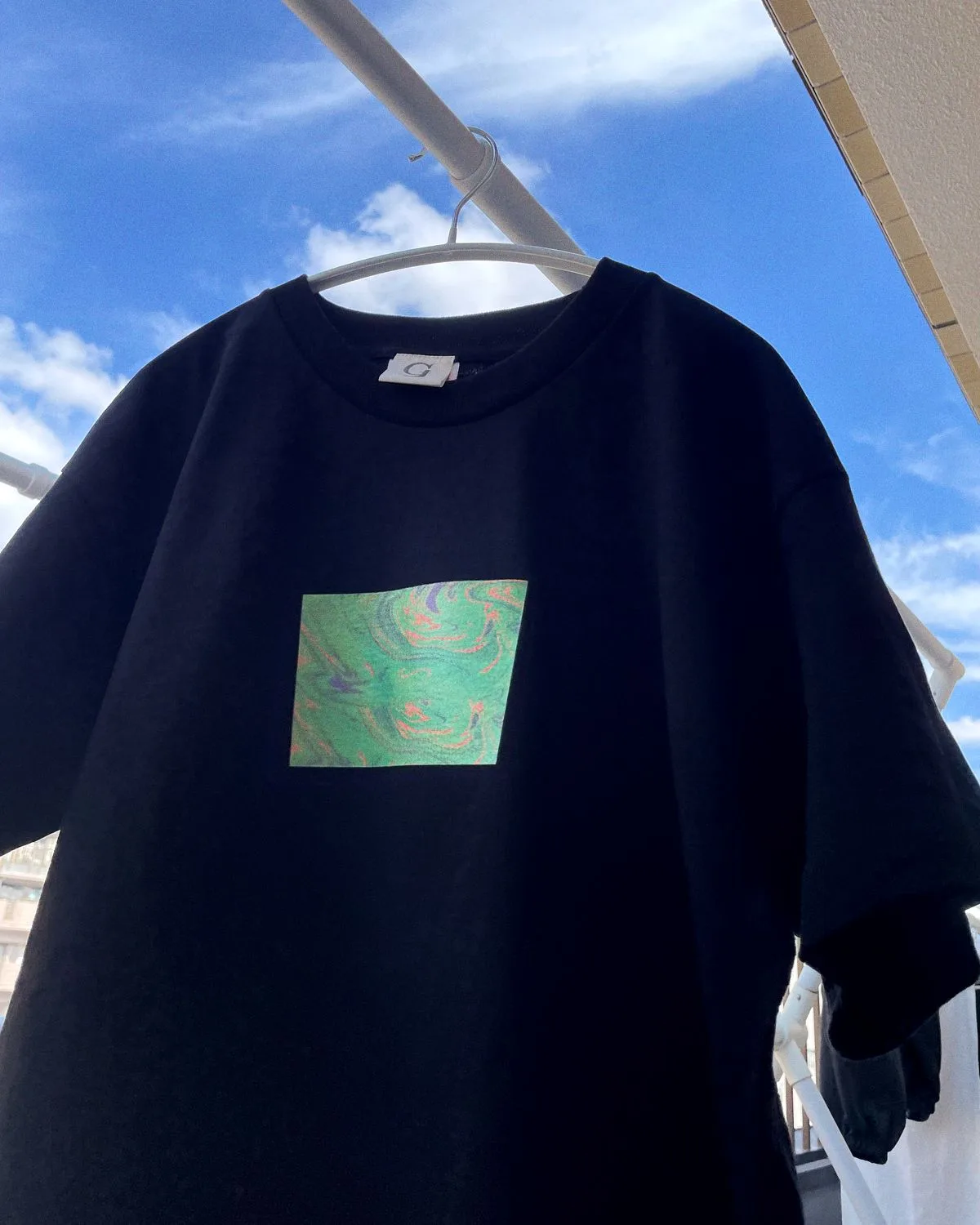 ORIGIN TEE(ブラック)。空を背景にハンガーに掛けた正面